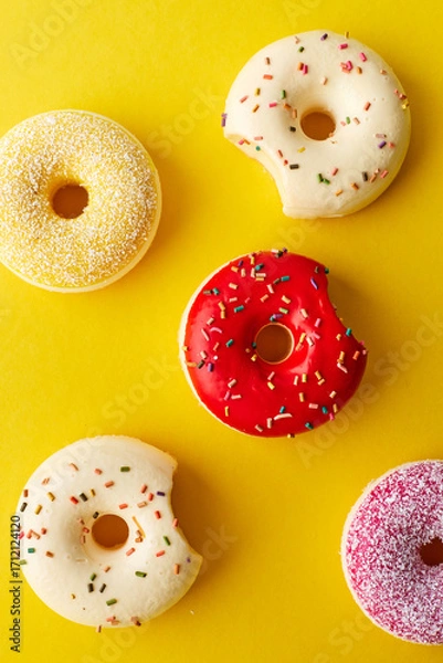 Fototapeta Overhead view of various donuts with confetti arranged on colored background
