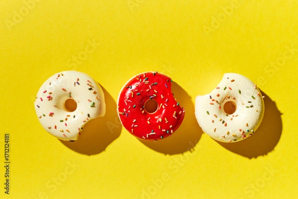 Fototapeta Overhead view of various donuts with confetti arranged on colored background