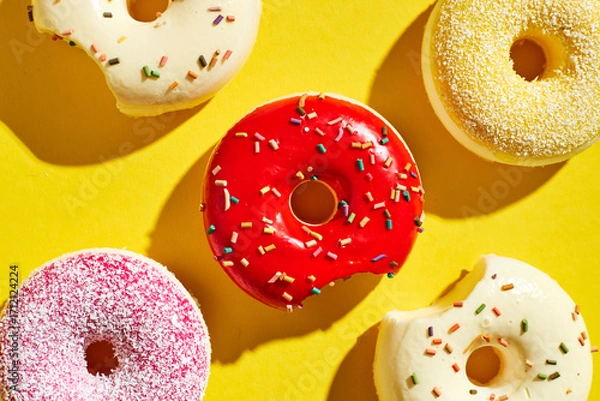 Fototapeta Overhead view of various donuts with confetti arranged on colored background