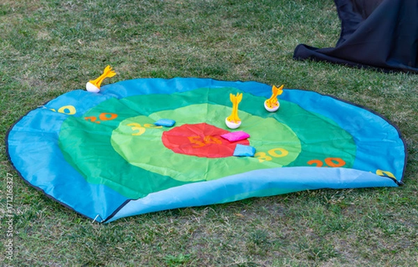 Fototapeta Colorful mat for darts skill game placed on grass, with scoring zones and soft throwing elements for outdoor play.