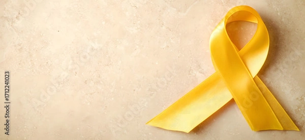 Fototapeta Yellow ribbon on flat yellow background, symbolizing cancer awareness with copy space for health campaigns and design use
