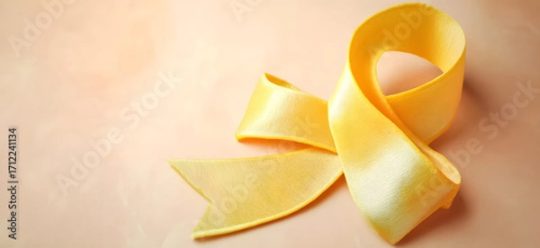 Fototapeta Yellow ribbon on flat yellow background, symbolizing cancer awareness with copy space for health campaigns and design use
