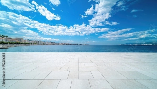 Obraz A wide-angle shot of an empty square floor with white tiles, overlooking the sea and blue sky with clouds in the summer. The city skyline is visible on the horizon.