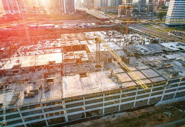 Fototapeta Construction Crane on Housing, drone view. Construction site with buildings under construction on sunset. Tower Crane during formworks. Multi Storey Residential Buildings construction, aerial view.
