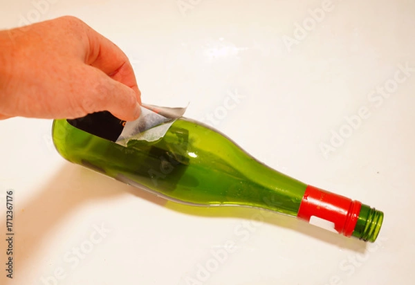 Fototapeta Removing label from bottle. Removing Wine Bottle Labels. Remove Old Wine Label. Sticker removers. Wine Label Removal. Glass for recycling. Soft focus.