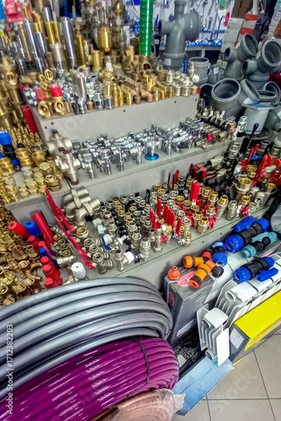 Fototapeta Assortment of plumbing supplies in hardware store, including fittings, valves, pipes, connectors, hoses, and tools. Various metal and plastic components organized on display shelves.