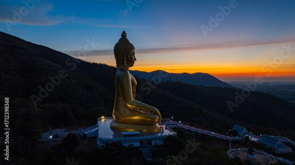 Fototapeta An awe-inspiring view of a big golden Buddha statue atop a hill overlooking a serene valley, captured during the vibrant colors of sunset. aerial view of The biggest golden Buddha at Lopburi Thailand