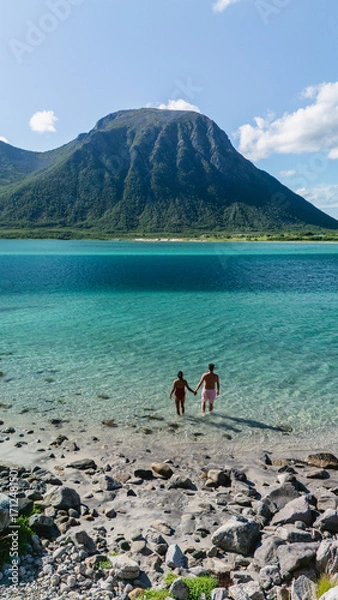 Fototapeta A couple stands hand-in-hand in the tranquil waters of a picturesque beach in Lofoten, Norway.