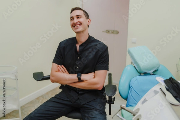 Obraz The smiling doctor in the dentist's office. Specialist in oral cavity treatment. A doctor in a black uniform. A doctor with a watch on his right hand.
