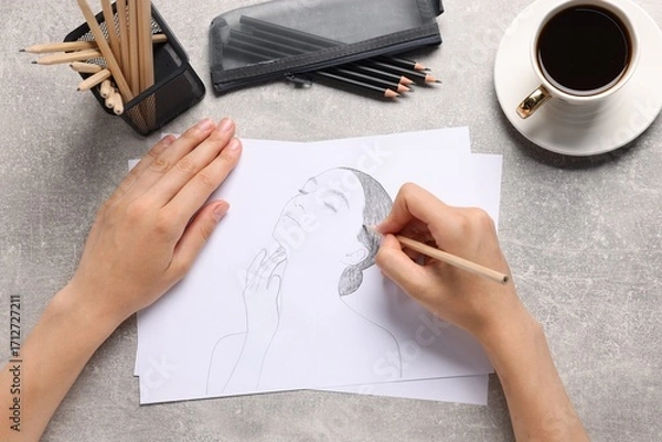 Fototapeta Woman drawing portrait sketch at grey table, top view