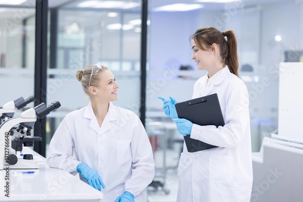 Fototapeta Scientists collaborate in a modern laboratory, sharing results and analyzing data on a tablet