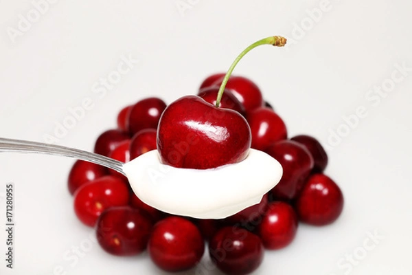 Fototapeta Teaspoon with cream and cherry on a white background