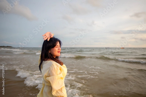 Obraz Beautiful Asian woman is happily strolling along the beach as the waves crash against her back. Happy girl rejoices in summer vacation.