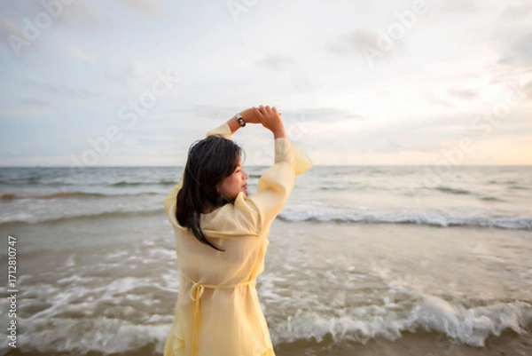 Obraz Beautiful Asian woman is happily strolling along the beach as the waves crash against her back. Happy girl rejoices in summer vacation.