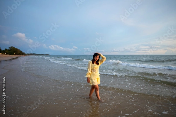 Obraz Beautiful Asian woman is happily strolling along the beach as the waves crash against her back. Happy girl rejoices in summer vacation.