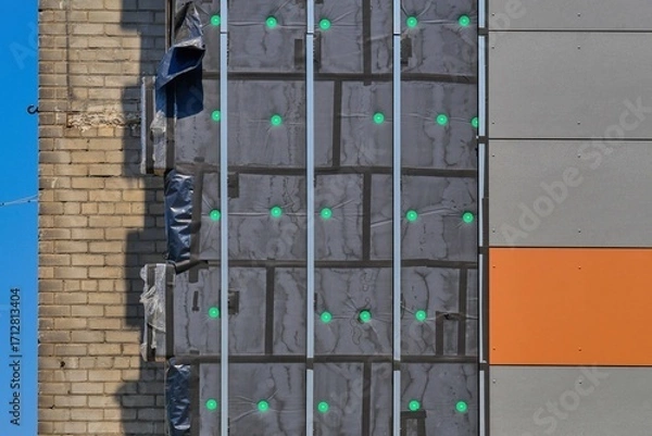 Fototapeta Thermal insulation installation on a building facade. Wall with mineral wool insulation, vapor barrier film, and metal frame for facade panels during construction or renovation.