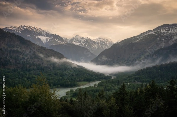 Fototapeta Snow-covered mountain range shrouded in mist under a cloudy sky, evoking a tranquil and enigmatic mood