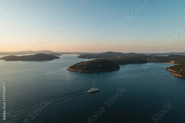 Fototapeta Gentle radiance bathes a peaceful cluster of wooded islets with a solitary vessel navigating serene waters, highlighting the expansive sky and ocean.