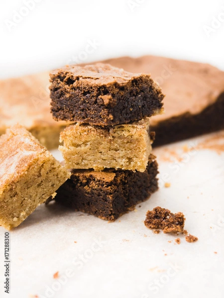 Fototapeta Stack of freshly baked brownies and snickerdoodle blondies squares on white baking parchment paper