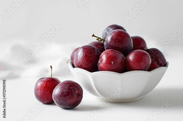 Fototapeta Close-up of mature plums arranged on a white plate with a white backdrop