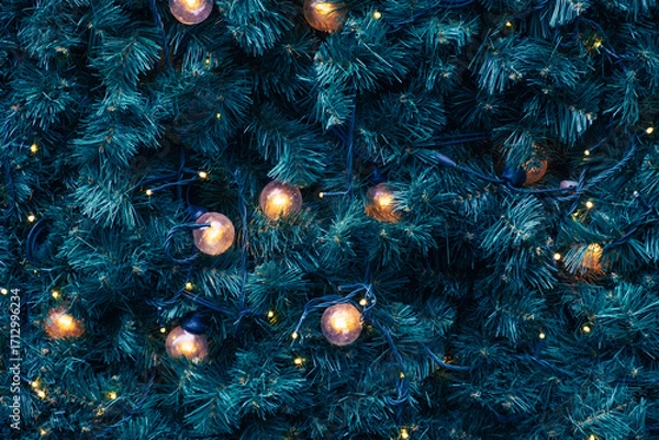 Fototapeta Warm glowing Christmas lights on green pine branches, festive background with golden bulbs and dark wiring, ideal for seasonal design or backdrop