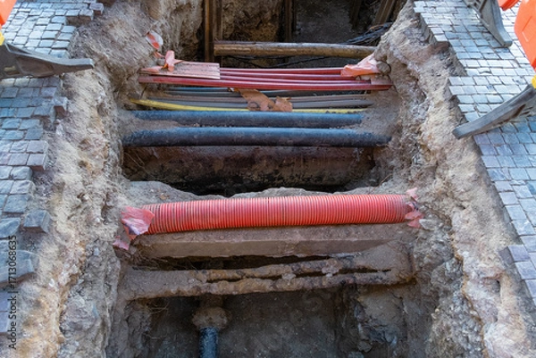 Fototapeta Various electrical wires are buried beneath a street walkway. Cobblestones are removed to allow underground cable installation