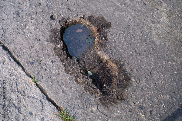 Fototapeta footprint shaped pothole is filled with rainwater on an concrete surface. damage of the road material