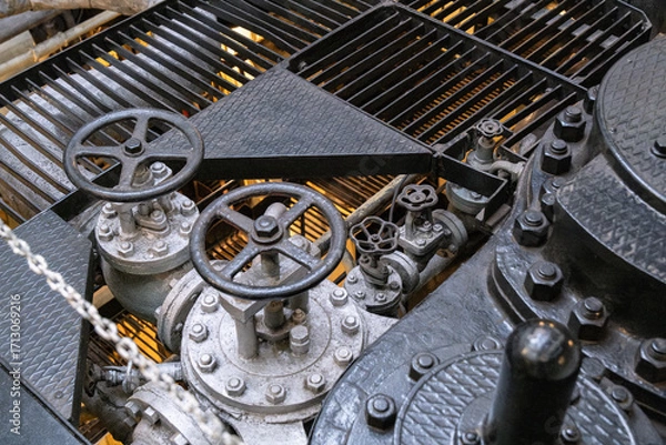 Fototapeta Steamship engine room – metal valves and wheels of a steam engine on a ship. Industrial mechanical system with pipes and controls.
