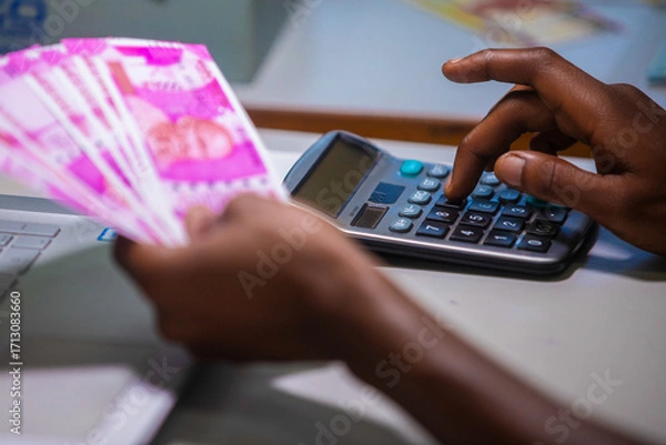 Fototapeta Dark skinned African person sitting punching pressing calculator with Indian Rupee notes on table desk