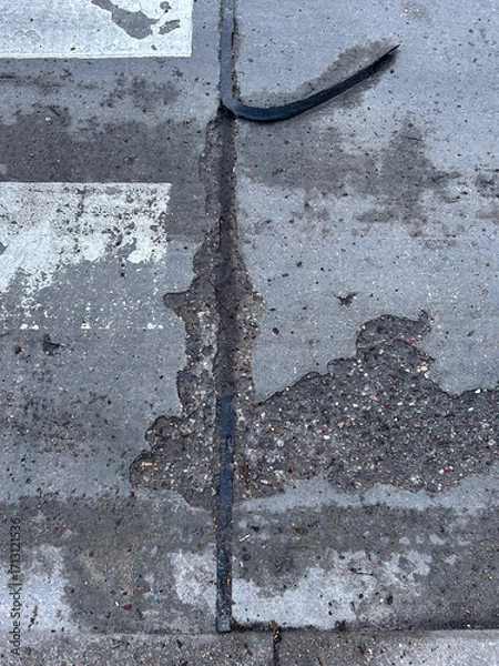 Fototapeta Close-up view of a damaged road surface with cracks and exposed asphalt lines.