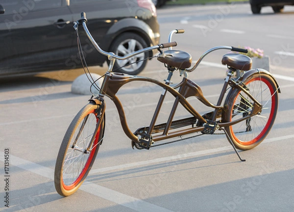 Fototapeta A tandem bicycle with scarlet wheel rims is parked in a parking lot in the evening sun.