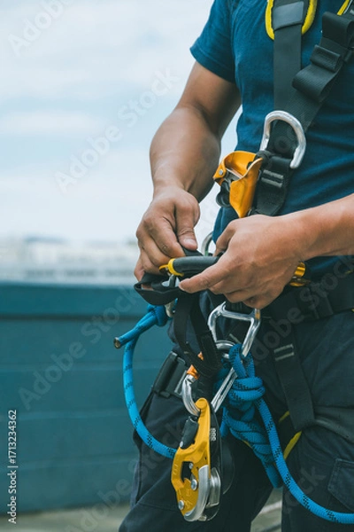 Fototapeta Firefighter and rescuer putting on harness, carabiners, and rappelling equipment to practice rappelling down a multi-story building.