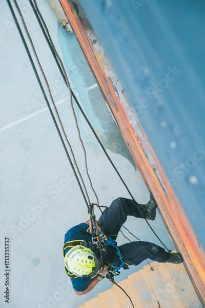 Fototapeta 
Firefighter rescuer descending a massive wall using a rappelling device in a multi-story building, wearing protective gear such as a helmet, harness, and carabiners.