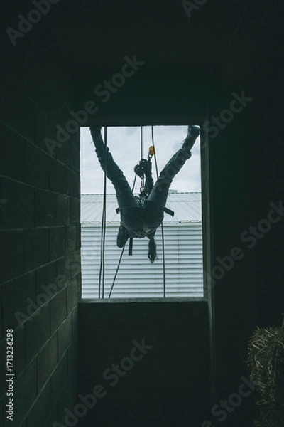 Fototapeta Female firefighter rescuer descending a huge wall with the rappelling device in a multi-story building, hanging from a window.