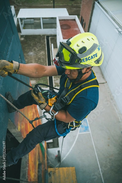 Fototapeta 
Firefighter rescuer descending a massive wall using a rappelling device in a multi-story building, wearing protective gear such as a helmet, harness, and carabiners.