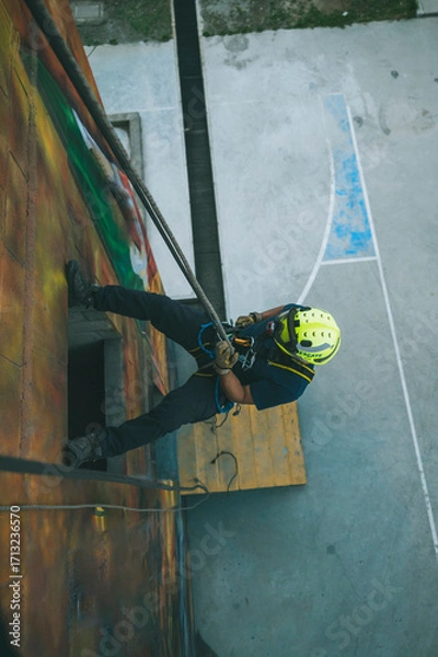 Fototapeta 
Firefighter rescuer descending a massive wall using a rappelling device in a multi-story building, wearing protective gear such as a helmet, harness, and carabiners.