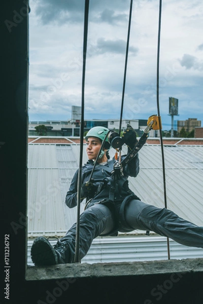 Fototapeta Female firefighter rescuer descending a huge wall with the rappelling device in a multi-story building, hanging from a window.