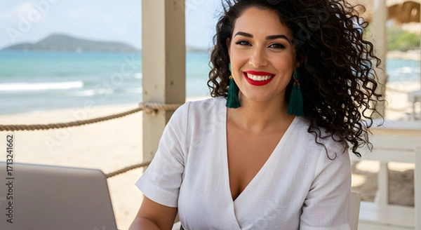 Obraz Smiling woman with curly hair working on laptop at a beachside cafe