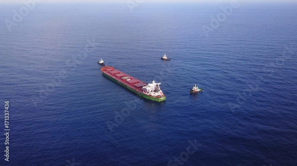 Obraz Large bulk carrier ship pulled by tugboats in open water