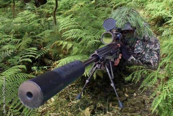 Fototapeta Military sniper wearing a camouflage waiting and looking through a rifle scope.