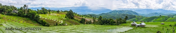 Fototapeta Panoramiczny widok na okoliczne domy i taras ryżowy w pochmurnym świetle w otoczeniu drzew i gór z ulewną burzą w tle w Pa Bong Piang Mae Chaem, Chiangmai, Tajlandia ...