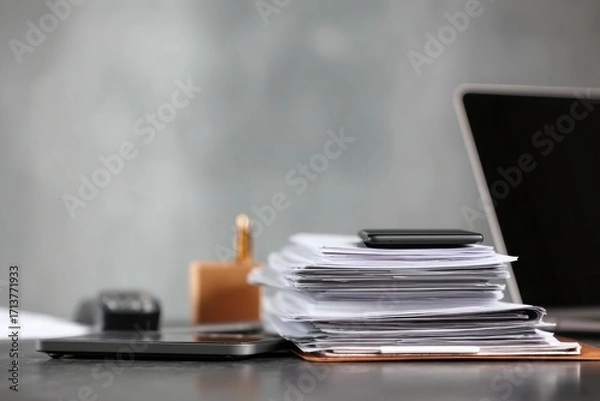 Fototapeta close-up of a desk in an office with documents, a laptop, and a phone on it, against a gray background, minimalistic style.