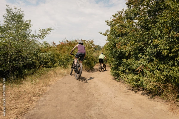 Fototapeta Cyclists enjoying a ride on outdoor trail surrounded by trees and nature beauty.