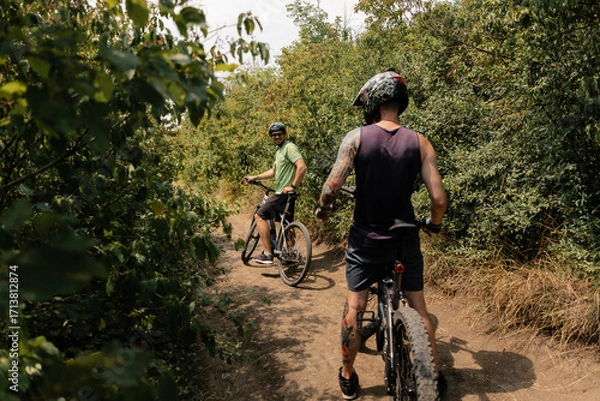 Fototapeta Two men riding bicycles on a natural path surrounded by greenery and trees