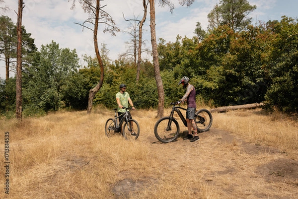 Fototapeta Two individuals with bicycles in a forest taking a break under sunny skies.