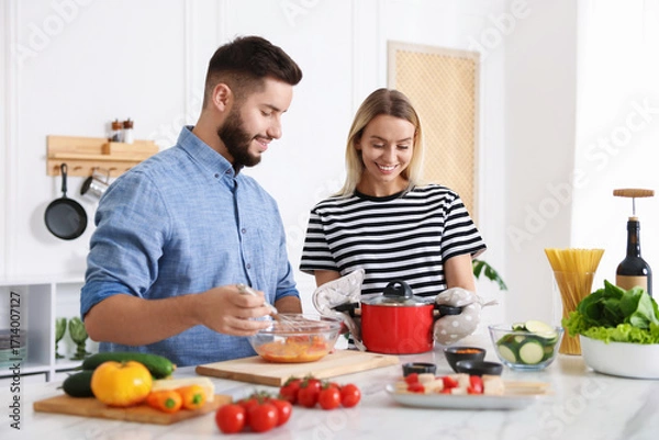 Fototapeta Happy couple cooking together at table in kitchen