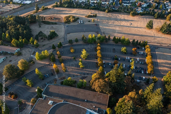 Fototapeta Aerial drone photo of an empty parking lot in Oregon City with landscaped rows, trees showing fall colors, and golden sunset light creating long shadows across the pavement and walkways