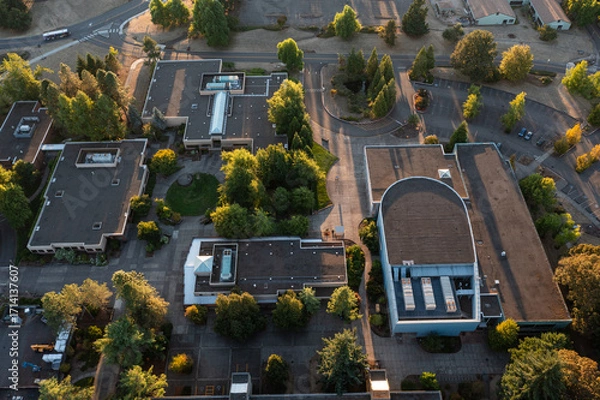 Fototapeta Aerial drone photo of a modern campus college area in Oregon City, USA, with surrounding trees and empty parking lots, captured during fall sunset with warm autumn colors and long evening shadows