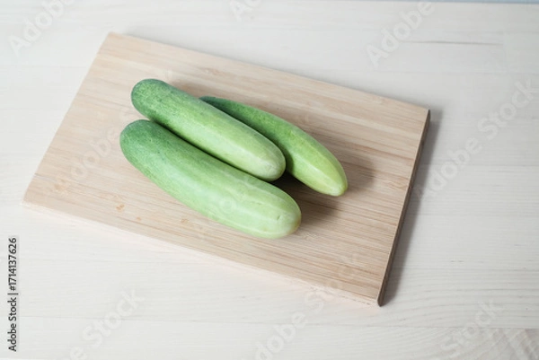 Fototapeta Fresh cucumber with cutting board on the wooden table.