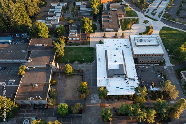 Fototapeta Aerial drone photo of a modern campus college area in Oregon City, USA, with surrounding trees and empty parking lots, captured during fall sunset with warm autumn colors and long evening shadows